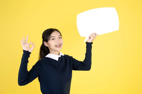 Asian teeanger holding white speech bubble on yellow background. — Stok fotoğraf