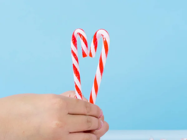 Ruka drží srdce tvar Vánoční cukroví tyčinka na modrém pozadí — Stock fotografie