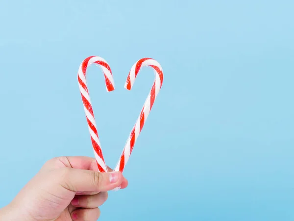 Main tenant forme de coeur bâton de bonbons de Noël sur fond bleu — Photo