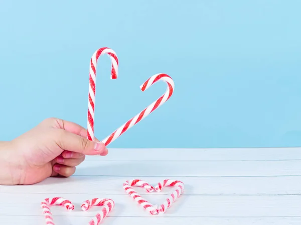 Tenuta a mano a forma di cuore bastone di caramelle di Natale sul backgroun blu — Foto Stock