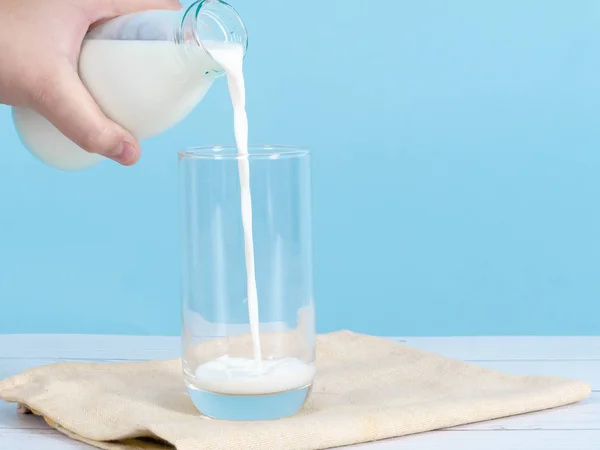Enfant main verser du lait dans du verre avec fond bleu . — Photo
