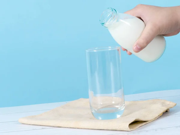 Enfant main verser du lait dans du verre avec fond bleu . — Photo