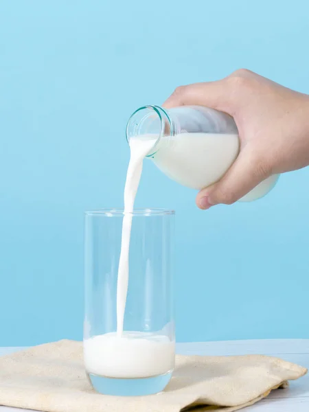 Enfant main verser du lait dans du verre avec fond bleu . — Photo