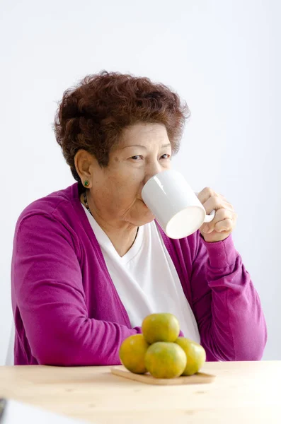 Asiatiska senior kvinna dricker en kopp te nära fönster med varma ligh — Stockfoto