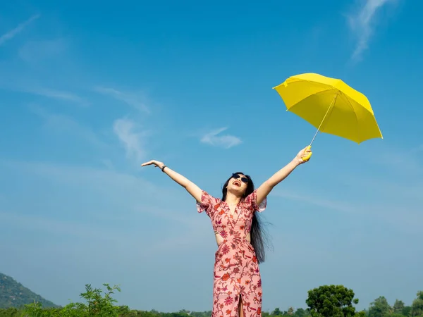 Happy Asian woman wearing sunglasses holding yellow umbrella aga — Stock Photo, Image