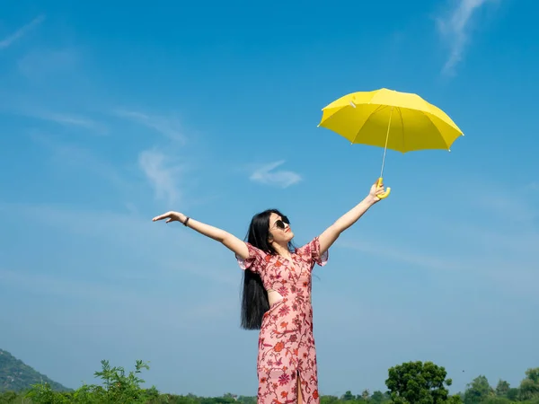 Felice donna asiatica indossa occhiali da sole tenendo ombrello giallo aga — Foto Stock