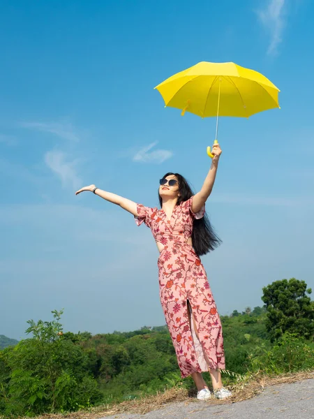Felice donna asiatica indossa occhiali da sole tenendo ombrello giallo aga — Foto Stock