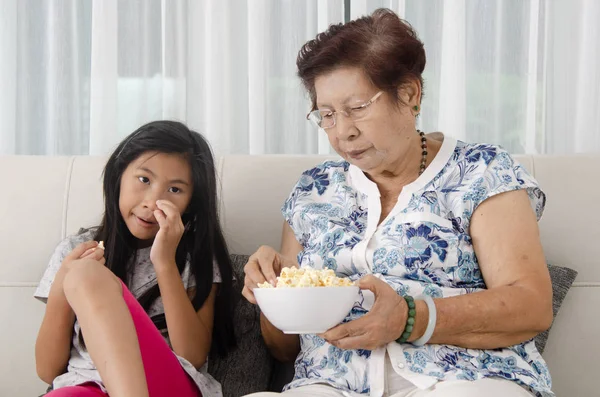 Asyalı kadın kıdemli onun torunu watc süre ile patlamış mısır yemek — Stok fotoğraf