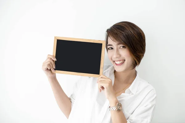 Beautiful woman holding blank blackboard with white wall. — Stock Photo, Image