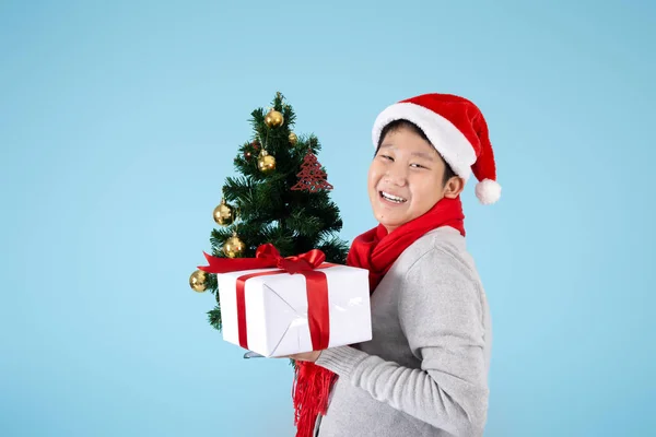 Happy Asian preteen boy holding Christmas tree and gift box on b Stock Image