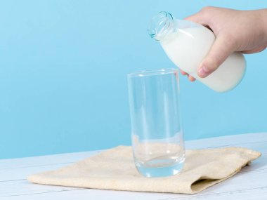 Çocuk eli mavi arka planlı bardağa süt döküyor..