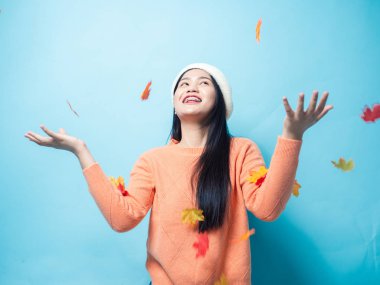 Mutlu Asyalı kadın süveter giyiyor ve akçaağaç düşürmekle oynuyor.