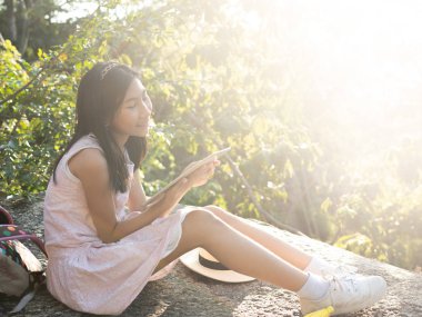 Doğada güneş ışığı ve yaşam tarzı olan tablet kullanan Asyalı bir kız.