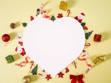 Beyaz kalp şeklindeki kağıt, sarı sırtüstü duran Noel nesneleri üzerine