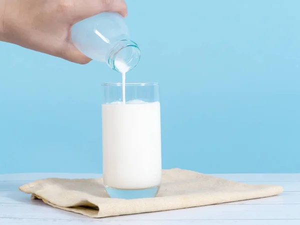Enfant main verser du lait dans du verre avec fond bleu . — Photo