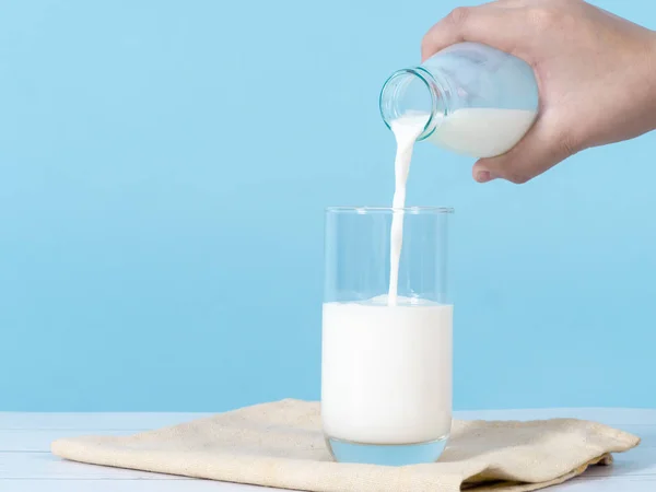 Kid mão derramando leite em vidro com fundo azul . — Fotografia de Stock