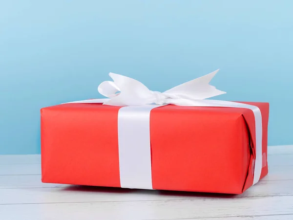 Rote Geschenkbox auf Holztisch mit blauer Wand. — Stockfoto