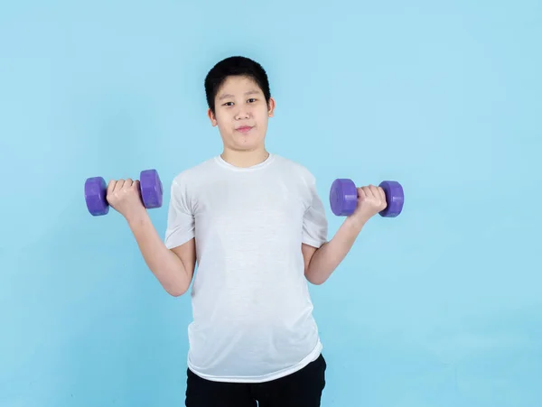 Smiling Asian boy using dumbbell on blue background. — Stock Photo, Image