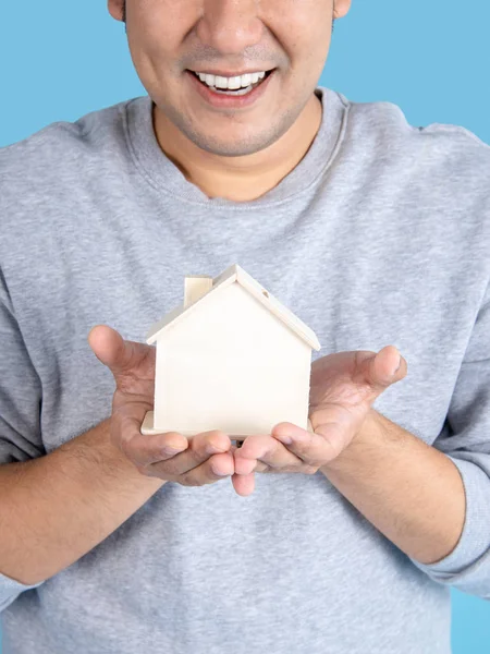 Man som håller trä hus leksak i handen, blå bakgrund. — Stockfoto