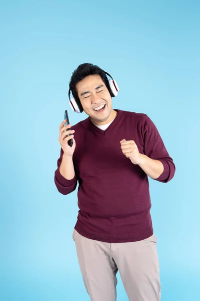 Mutlu Asyalı adam kulaklık ve akıllı telefon kullanarak kazak giyiyor. — Stok fotoğraf