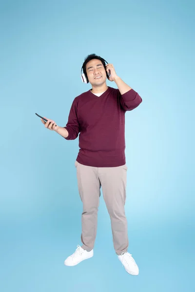 Homem asiático feliz vestindo camisola usando fone de ouvido e smartphone — Fotografia de Stock