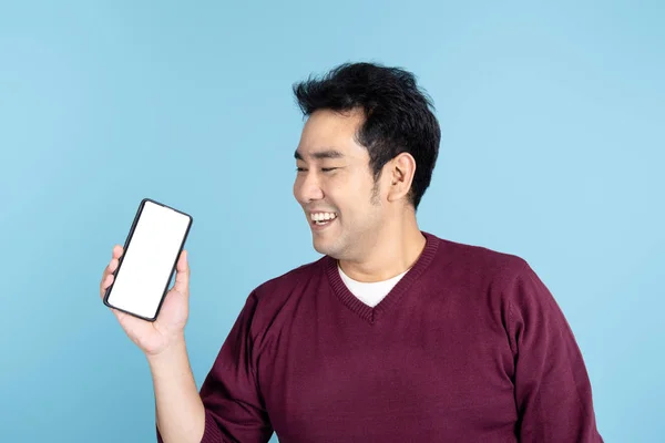 Happy Asian man wearing sweater holding black smartphone on blue — Φωτογραφία Αρχείου