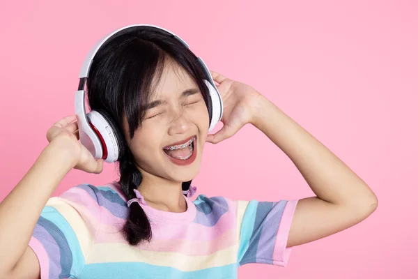 Gelukkig aziatische tiener meisje met behulp van hoofdtelefoon op roze achtergrond. — Stockfoto