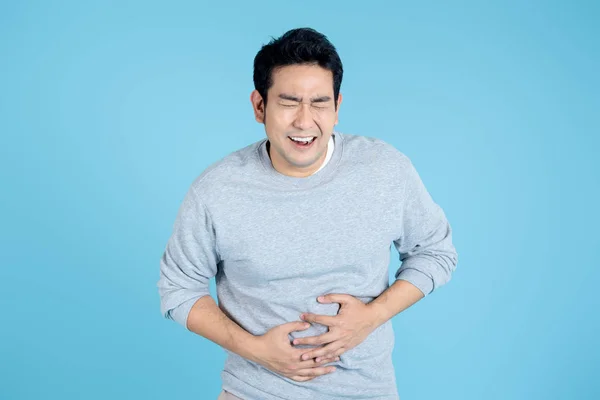 El hombre asiático que tiene stomachache en el fondo azul, concepto de salud. —  Fotos de Stock