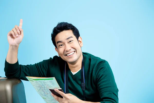 Glad asiatisk turist sitter och läser karta på blå bakgrund, — Stockfoto