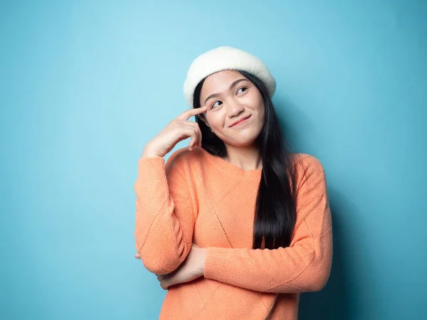 Mavi arka planda turuncu süveter giyen düşünceli Asyalı kadın. — Stok fotoğraf