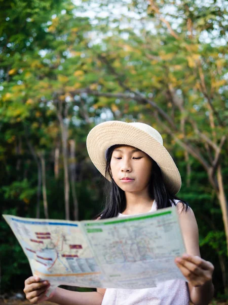 Young girl reading map with tree background, lifestyle concept.