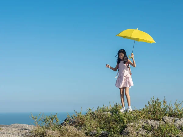Girl with backpack holding yellow umbrella climbing on the top o — Stock Photo, Image