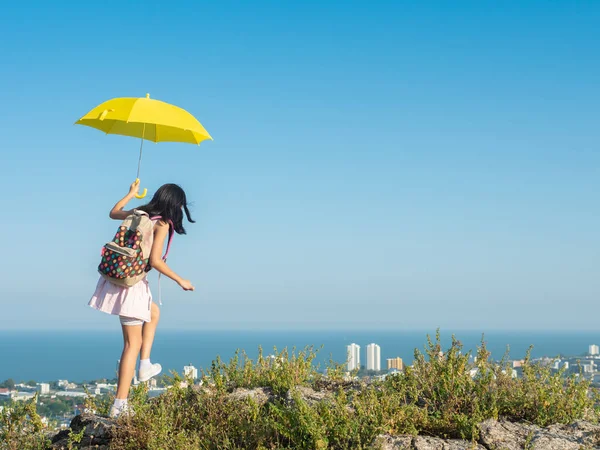 Girl with backpack holding yellow umbrella climbing on the top o — Foto Stock