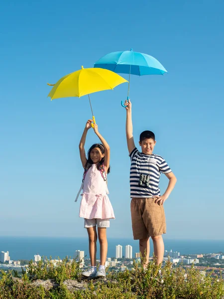 Asian preteen boy and girl holding yellow and blue umbrella with — Foto Stock