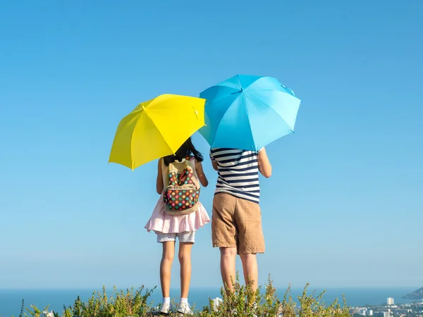 Back of boy and girl holding yellow and blue umbrella with top o — 스톡 사진