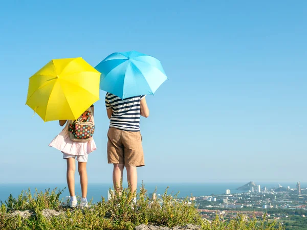 Back of boy and girl holding yellow and blue umbrella with top o — Foto de Stock