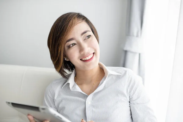 Portrait of a happy Asian woman sitting on sofa using Digital Ta — Stock Photo, Image