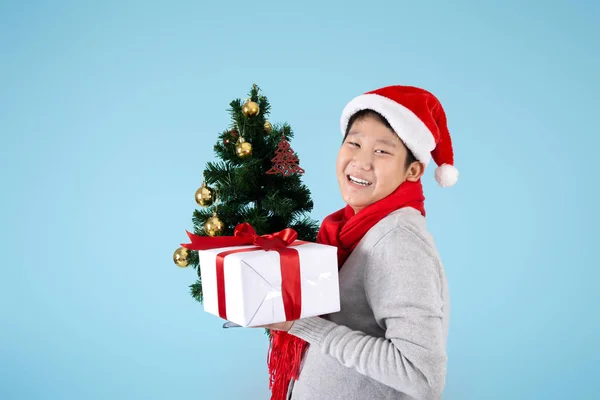 Happy Asian preteen boy holding Christmas tree and gift box on b Royalty Free Stock Images