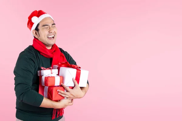 Happy Asian man wearing green sweater and Santa hat holding gift Royalty Free Stock Images