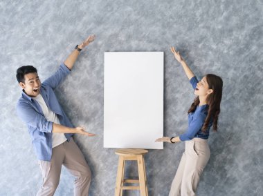 Mutlu Asyalı çift, gri sırtlı boş beyaz tahta sunar..