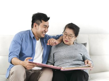 Asyalı bir adam ve annesi evde otururken birlikte fotoğraf albümüne bakıyorlar..