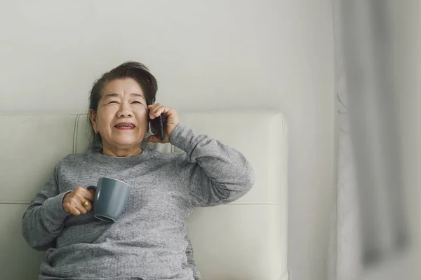 Szczęśliwy Azji Starszy Kobieta Mówi Telefon Trzymając Kubek Pić Pobyt — Zdjęcie stockowe
