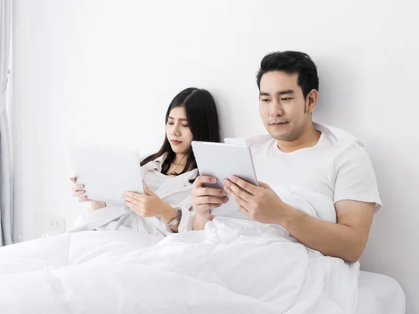 Happy Asian couple using tablet and laptop on bed, work from home, stay home stay safe concept.