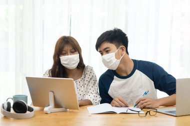 Asyalı genç bilgisayarını ve tabletini evden online eğitim için kullanıyor, karantina konsepti.
