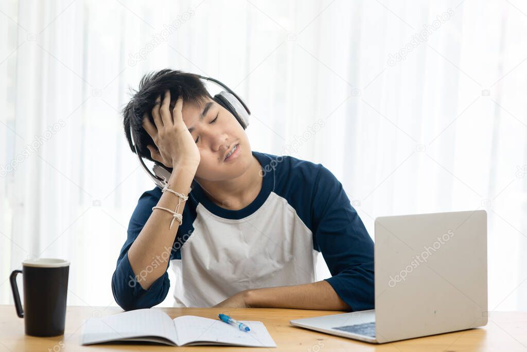 Asian teenager using headphone and laptop for online education, headache and seriously situation.