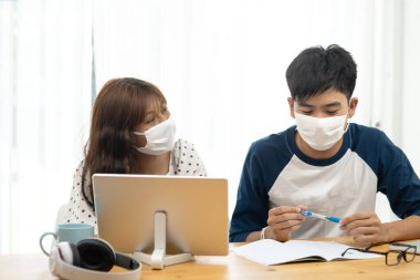 Asyalı genç bilgisayarını ve tabletini evden online eğitim için kullanıyor, karantina konsepti.