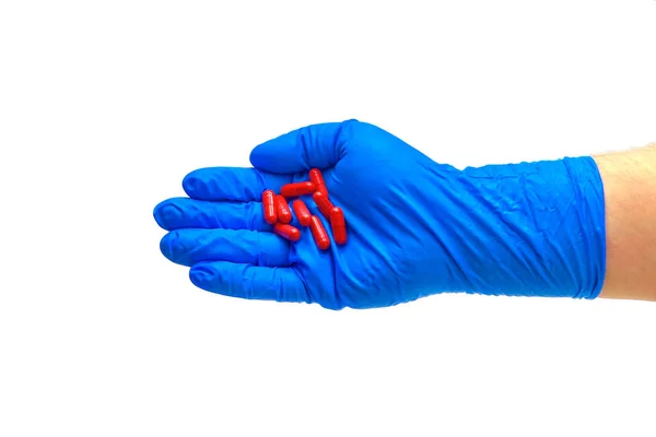 Un médico con guantes azules sostiene un puñado de pastillas rojas . — Foto de Stock