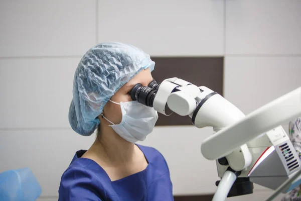 女牙医看着显微镜 通过牙科诊所的显微镜对病人进行治疗 — 图库照片