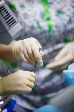 Tedavi ve protez sürecinde lastik eldivenlerin içindeki dişçi elleri. Diş aletleriyle doktor eli..