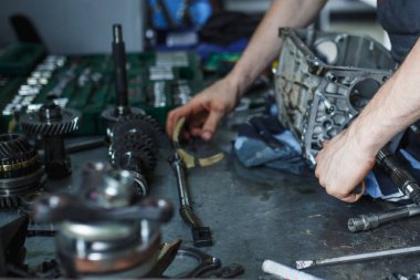 Servis istasyonunda araba tamiri. Direksiyonsuz asansörde arabayı tamir eden, lastiği tutan ve mekanik işleri tutan tulumda bir tamircinin elleri.